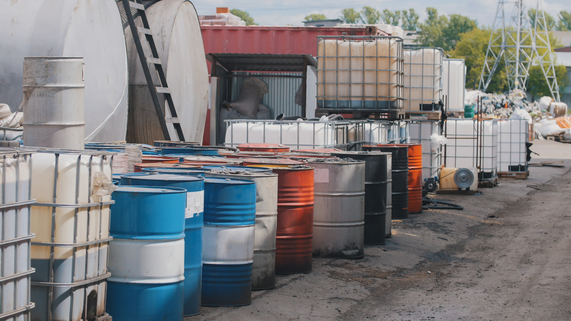 Steel drums and IBC totes staged at an industrial packaging yard — multi-mode petroleum and specialty oil packaging across APAC supply chains.